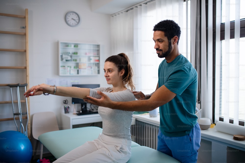 Um fisioterapeuta jovem examinando a paciente da jovem mulher em uma sala física
