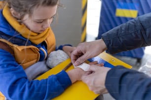 Un bénévole aide un enfant réfugié ukrainien à la gare, en train de panser sa main blessée.