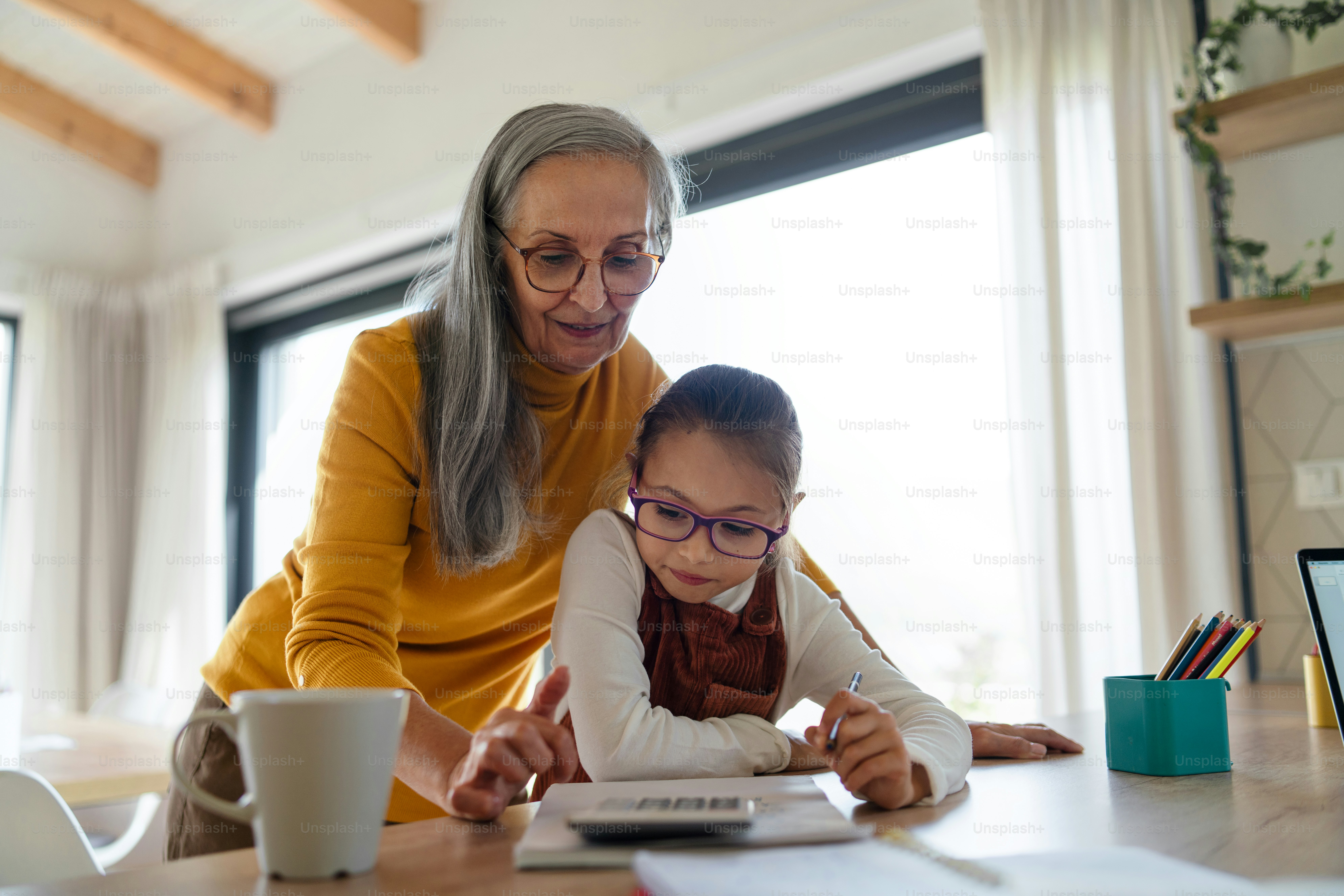 A small girl with senior grandmother doing homework at home. photo ...