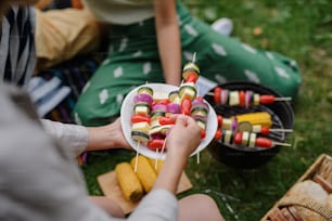 Close-up of young friends putting corn and skewers on grill and having barbecue when camping in campground.