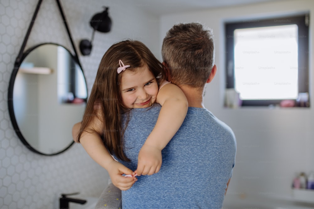 Eine Rückansicht des Vaters, der seine kleine Tochter im Badezimmer trägt, Morgenroutinekonzept.