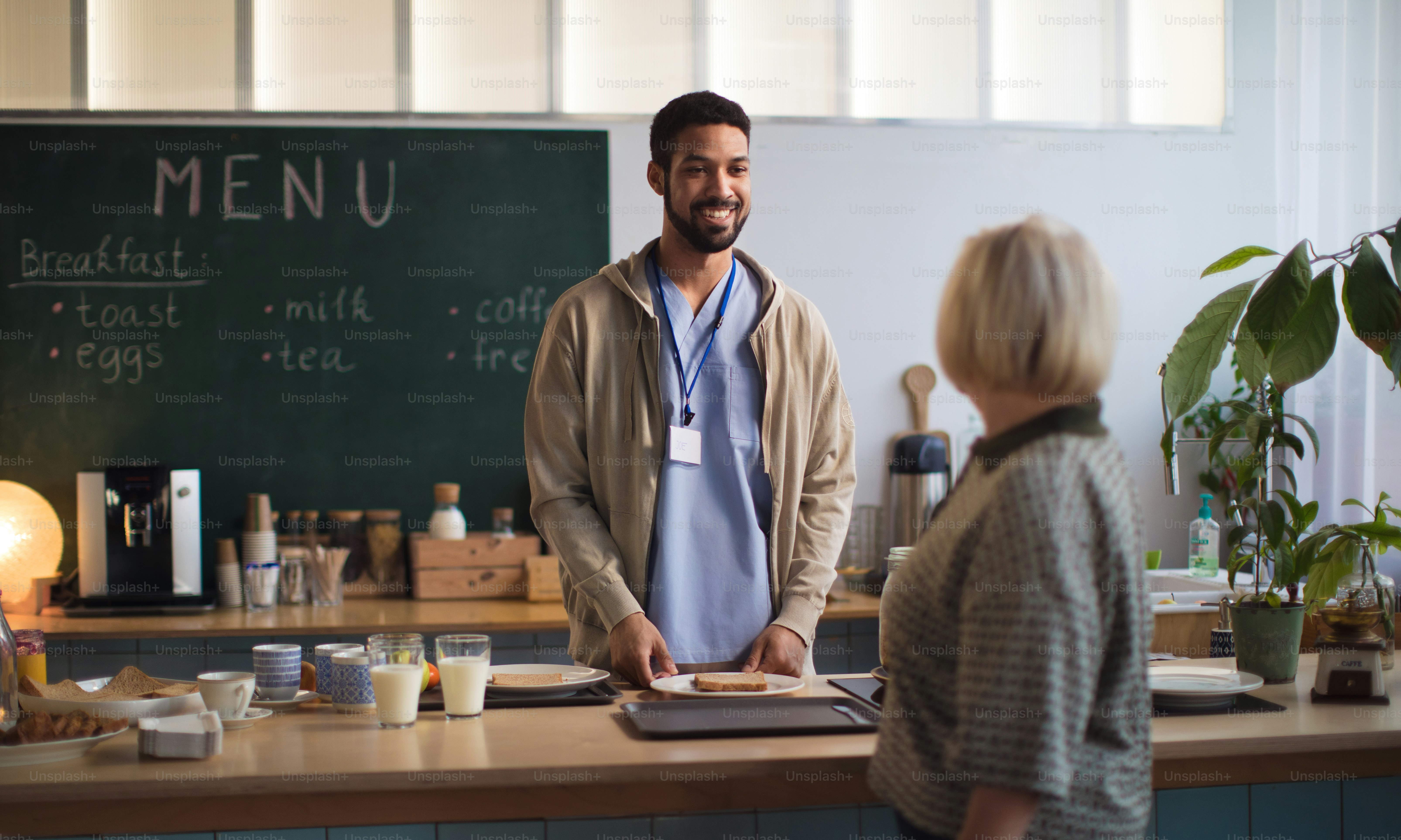 Eine junge Pflegekraft serviert älteren Frauen Frühstück im Pflegeheim.
