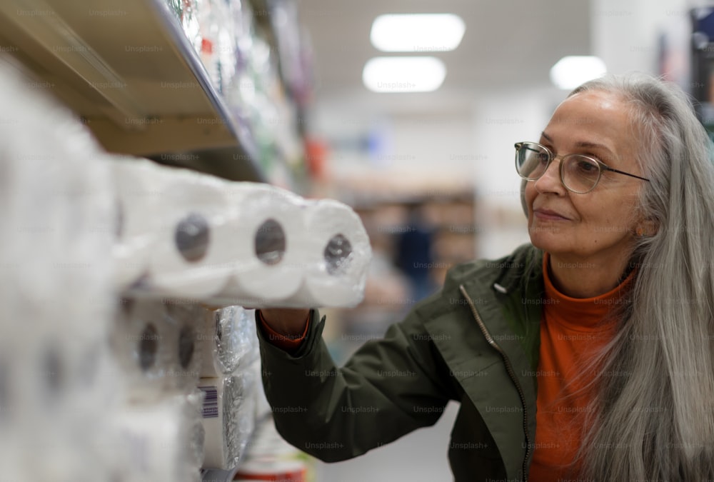 Una donna anziana che compra carta toliet al supermercato.