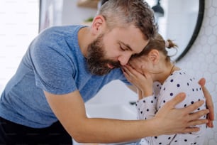 A father consoling his little upset daughter in bathroom at home.