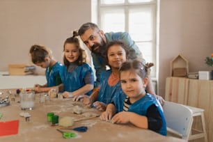 A group of little kids with teacher working with pottery clay during creative art and craft class at school.