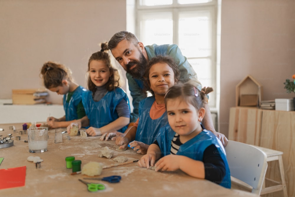 A group of little kids with teacher working with pottery clay during creative art and craft class at school.
