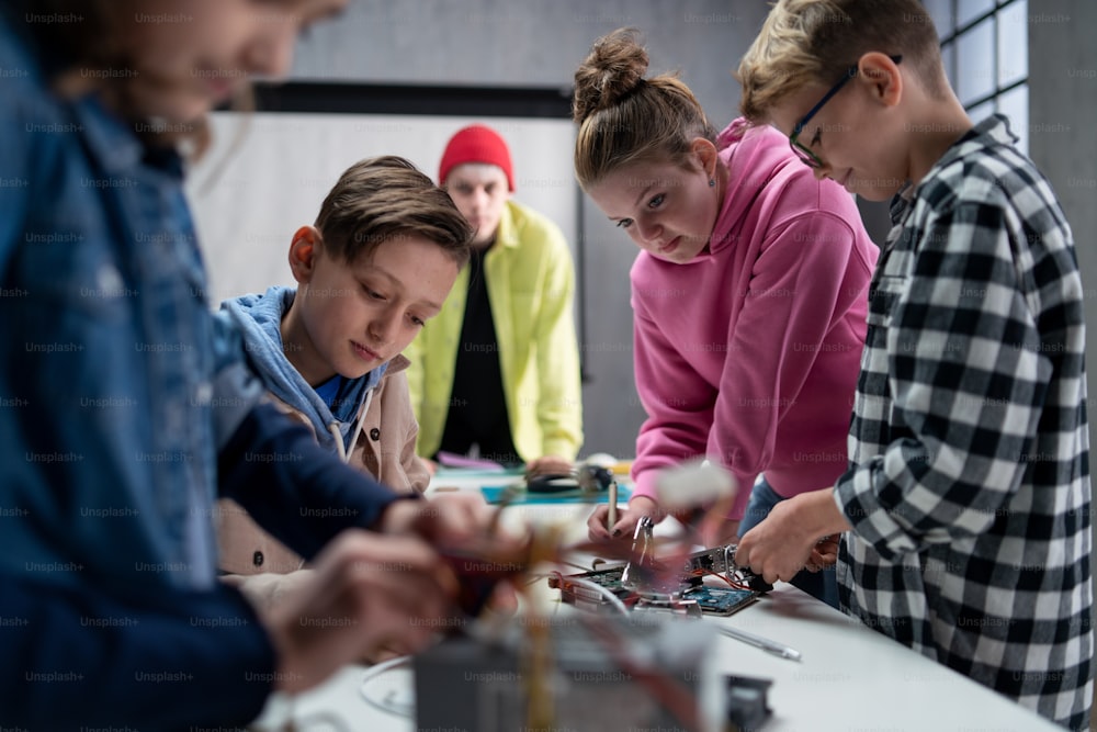 Eine Gruppe glücklicher Kinder mit ihrem Naturwissenschaftslehrer mit elektrischem Spielzeug und Robotern im Robotik-Klassenzimmer