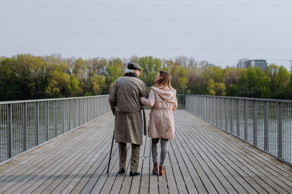川沿いの桟橋を散歩する娘を連れた年配の男性の後ろ姿。