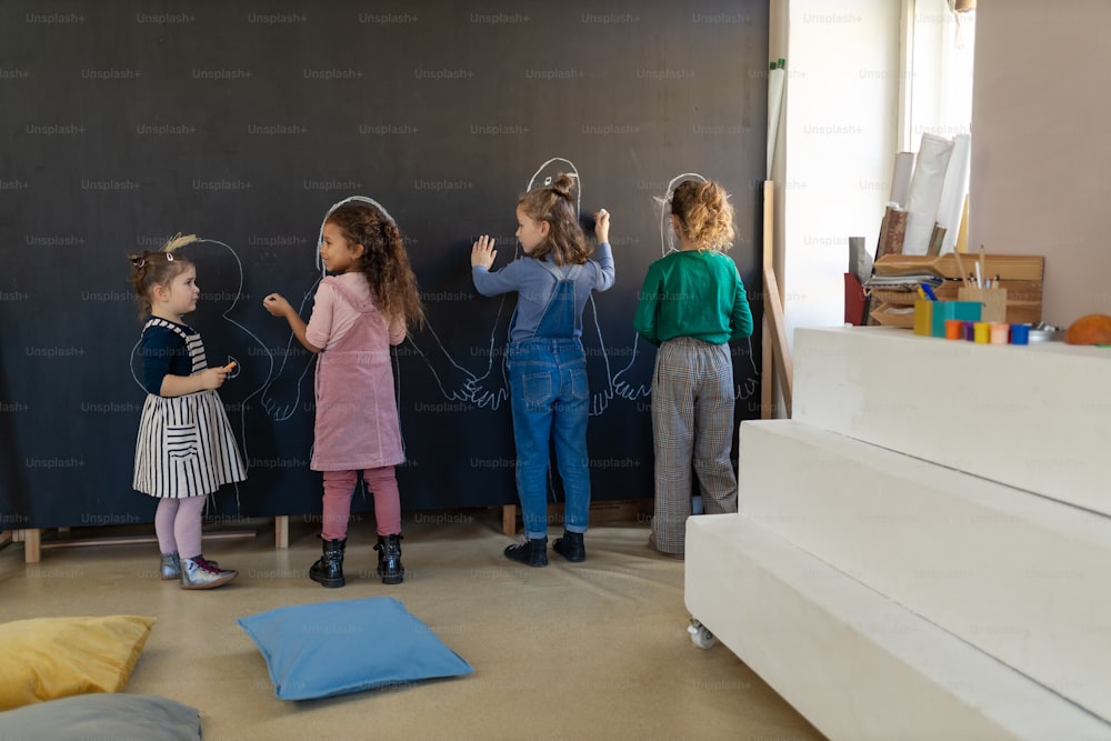 A group of little girls posing in front of blackboard wall paintings indoors in playroom.