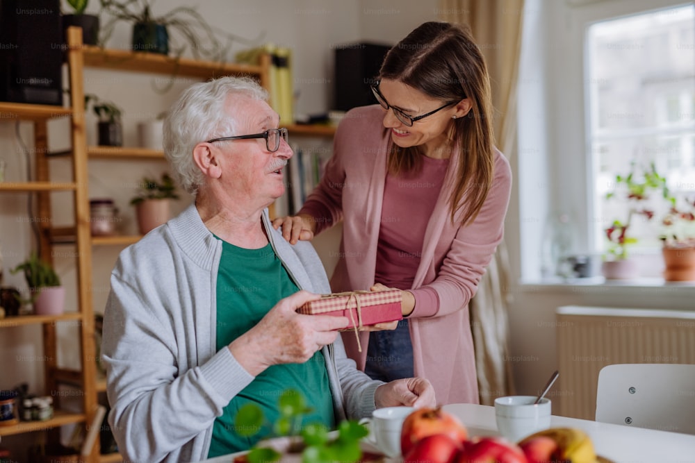 A happy woman surprising her senior father when visiting him at home and bringing present.