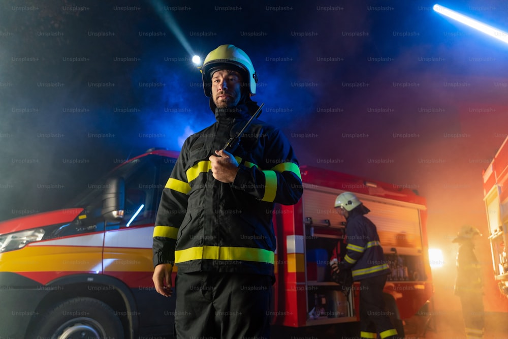 夜間に消防車を背景にトランシーバーに話しかける消防士のローアングルビュー。