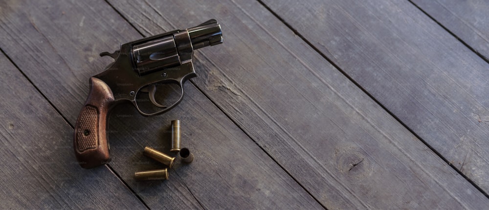 Um revólver com balas na mesa de madeira.