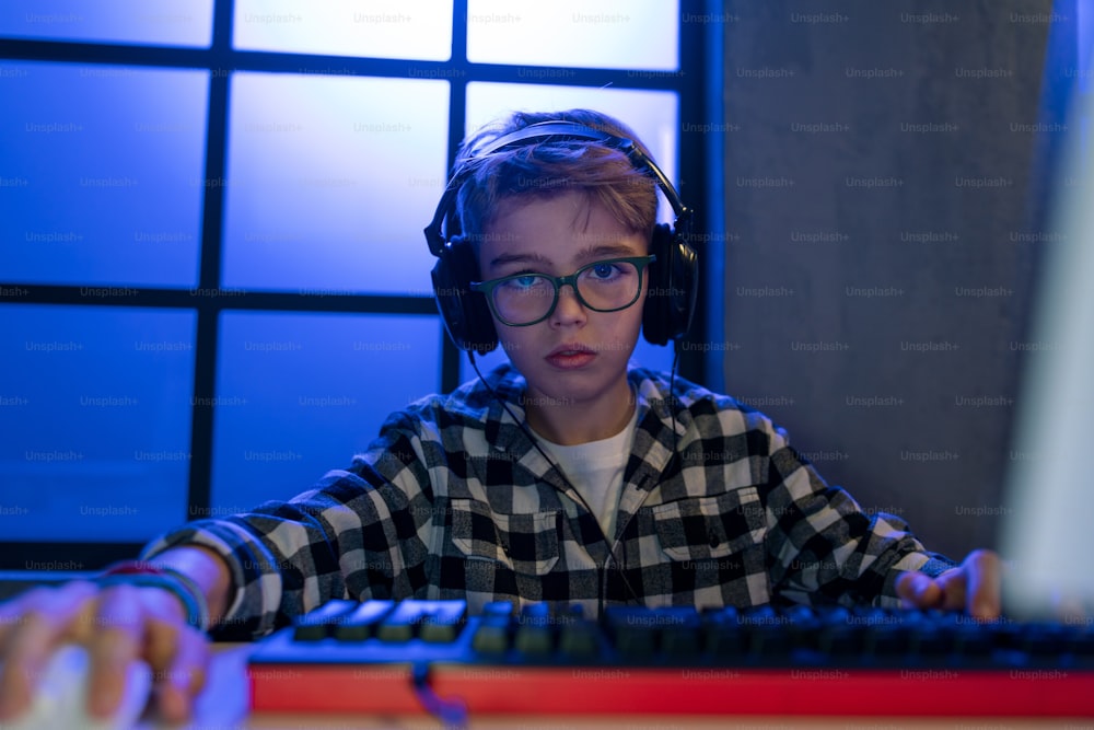 A young gamer boy with headphones playing computer video game.