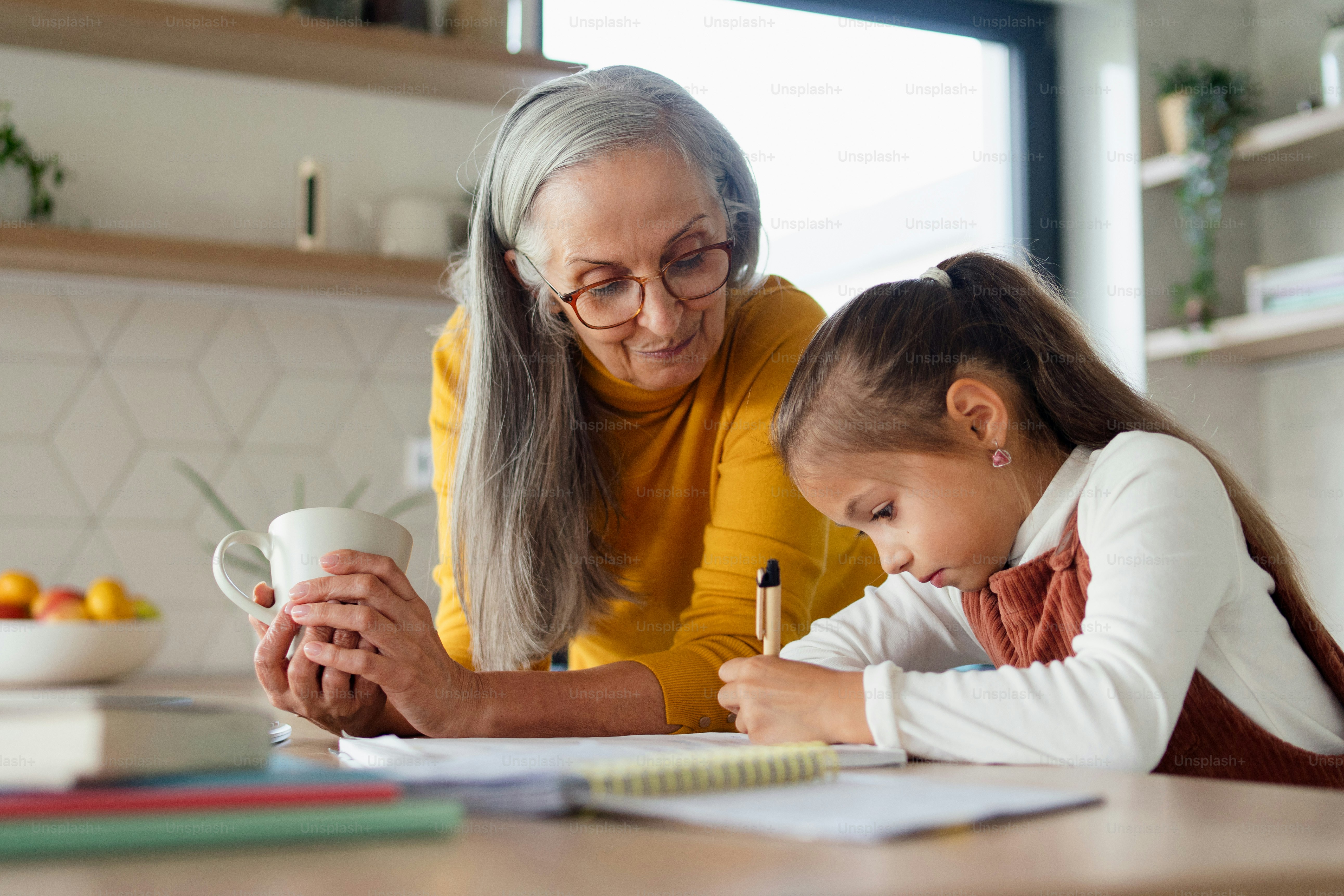 A small girl with senior grandmother doing homework at home. photo ...