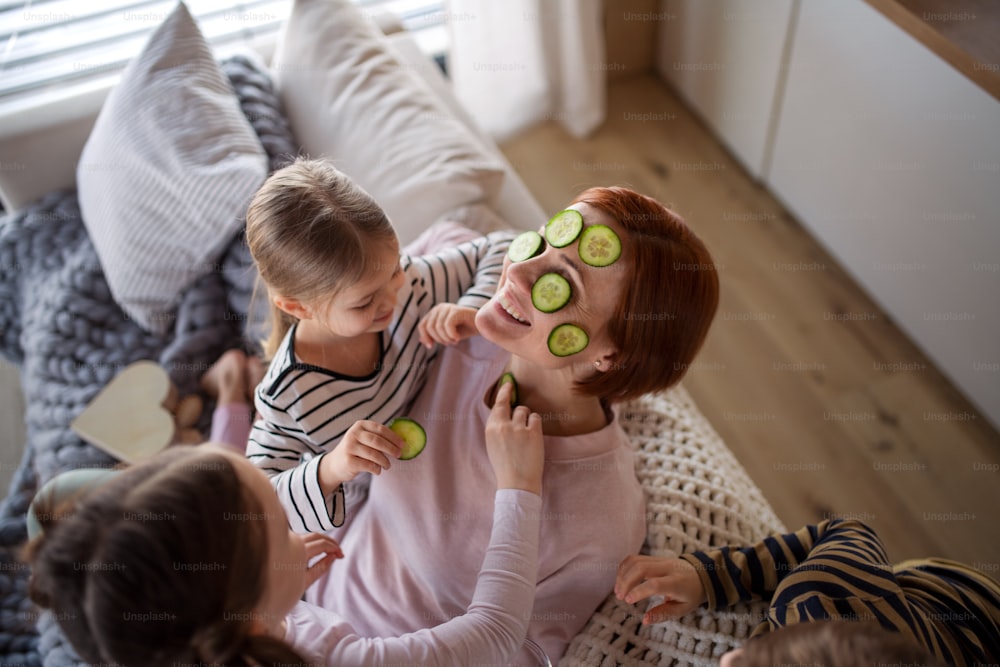 Three little children putting a cucumber on their mother's face at home.