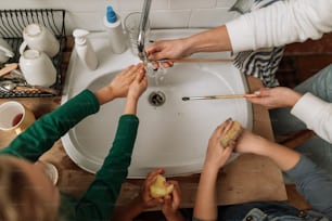 Close-up of little girls washing hands and brushes in washbasin after art class in school bathroom.