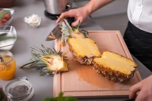 An unrecognizable man cutting a pineapple on chopping board.