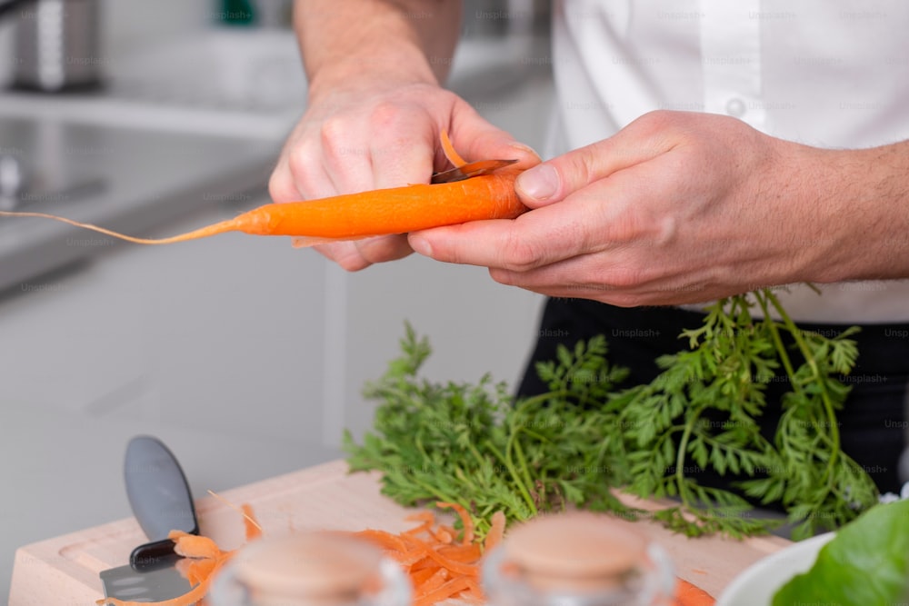 Um homem preparando refeição vegetariana descascando cenoura na tábua de corte. Refeição caseira
