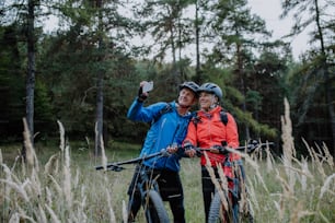 A senior couple bikers using smartphone outdoors in forest in autumn day.