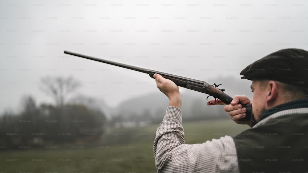 Un cacciatore in abiti da tiro tradizionali sul campo che mira con il fucile.