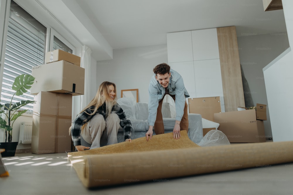A cheerful young couple in their new apartment, rolling out carpet. Conception of moving.