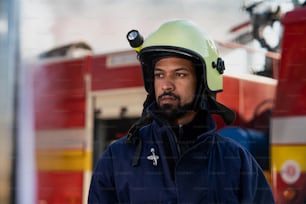 A serious young African-american firefighter man with fire truck and smoke in background.