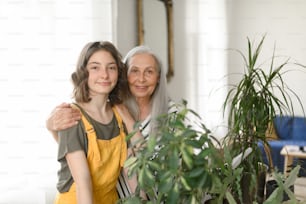A senior grandmother with teenage granddaguhter caring about plants together at home.