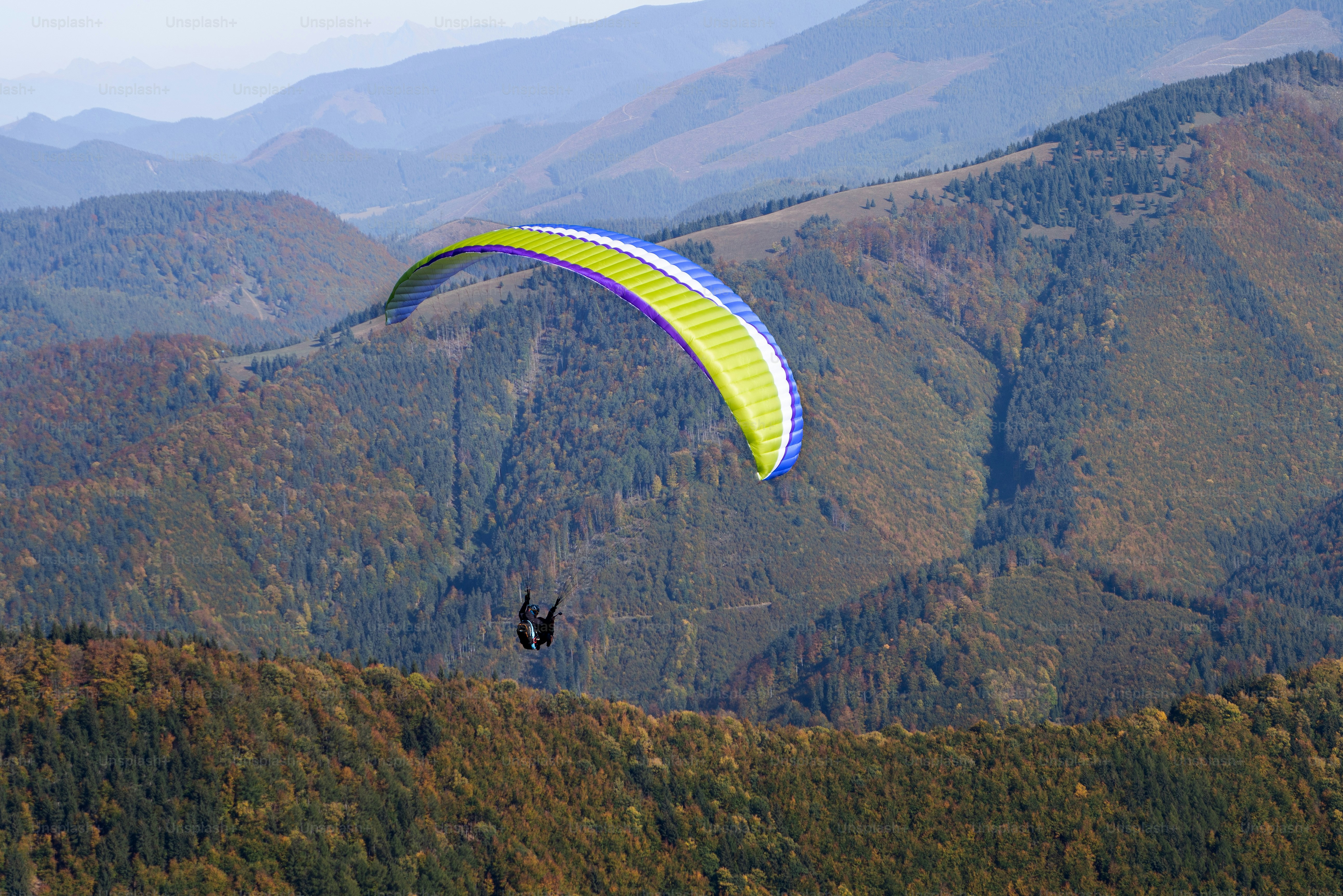 Gleitschirmflieger fliegen in einem blauen Himmel mit Berg im Hintergrund.