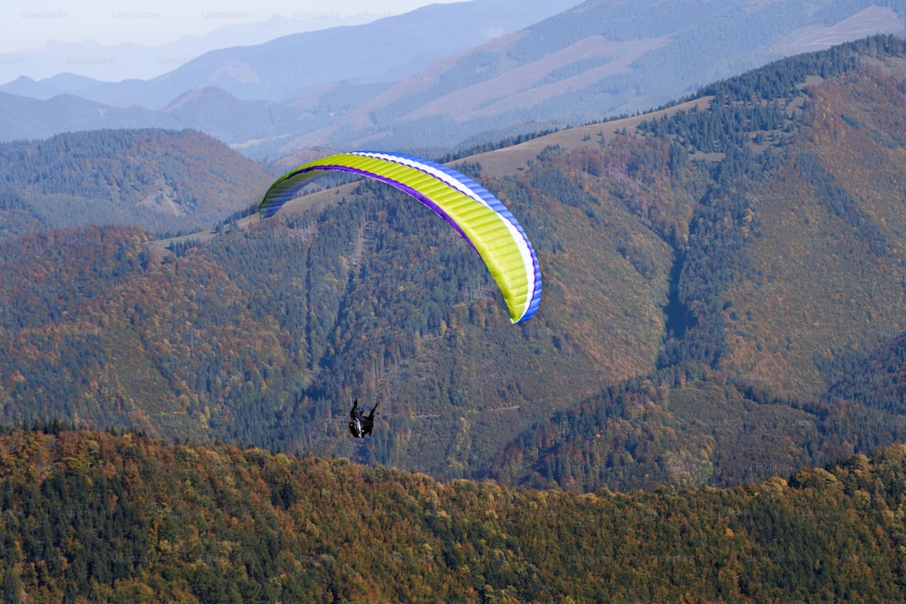 山を背景に青空を飛ぶパラグライダー。