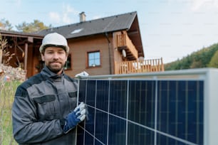 Un sorridente installatore solare tuttofare che trasporta un modulo solare durante l'installazione di un sistema di pannelli solari in casa.