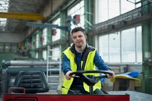Un joven con síndrome de Down que trabaja en una fábrica industrial, conduciendo una máquina de trabajo, concepto de integración social.