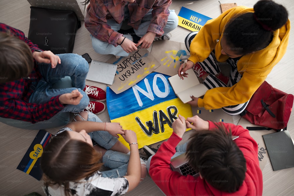 Draufsicht von jugendlichen Schülern, die im Kreis in einem Klassenzimmer sitzen, mit Plakaten zur Unterstützung der Ukraine, kein Kriegskonzept.