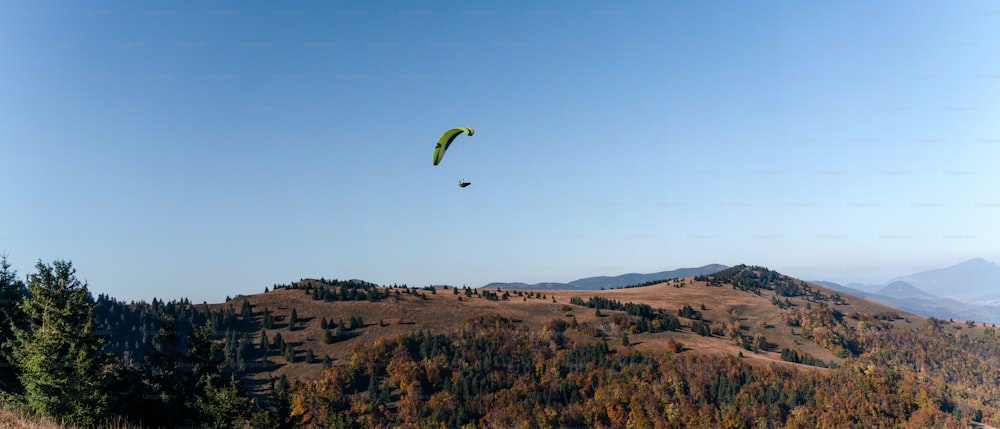 Um parapente voando no céu azul com a montanha ao fundo.