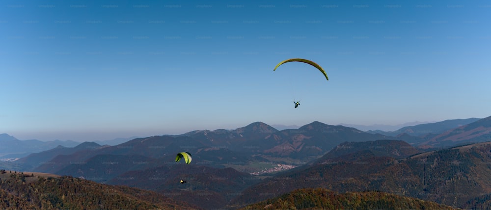 A paraglider flying in the blue sky with mountain in background.