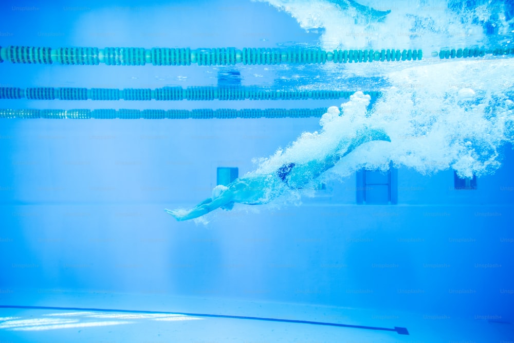 Senior man in an indoor swimming pool. Active pensioner enjoying sport. An old man jumping in the pool.