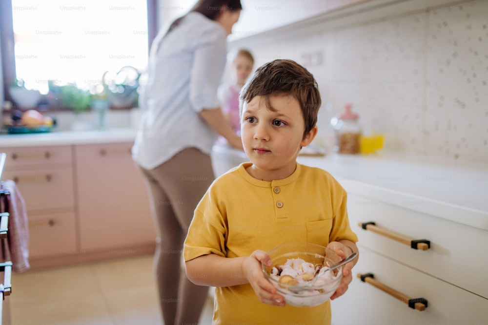 Um menino segurando tigela com café da manhã na cozinha em casa.