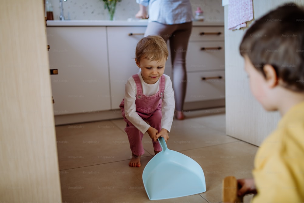 A little boy and girl helping to clean house using pan and brush as they sweep up dirt off floor.