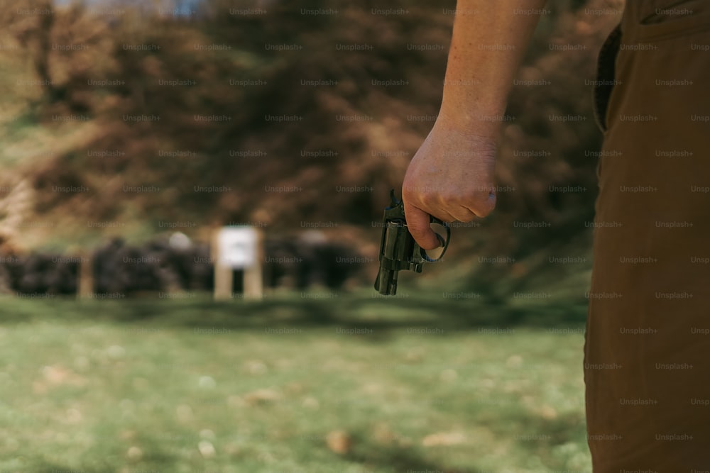 Un homme méconnaissable avec un revolver se préparant à tirer sur une cible sur un champ de tir à l’extérieur.