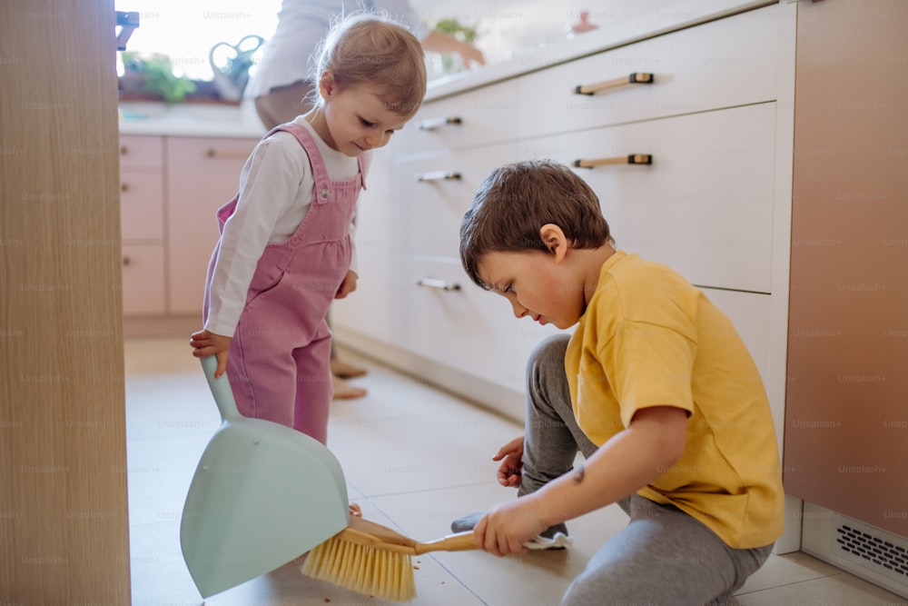 Un bambino e una bambina che aiutano a pulire la casa usando padella e spazzola mentre spazzano via lo sporco dal pavimento.
