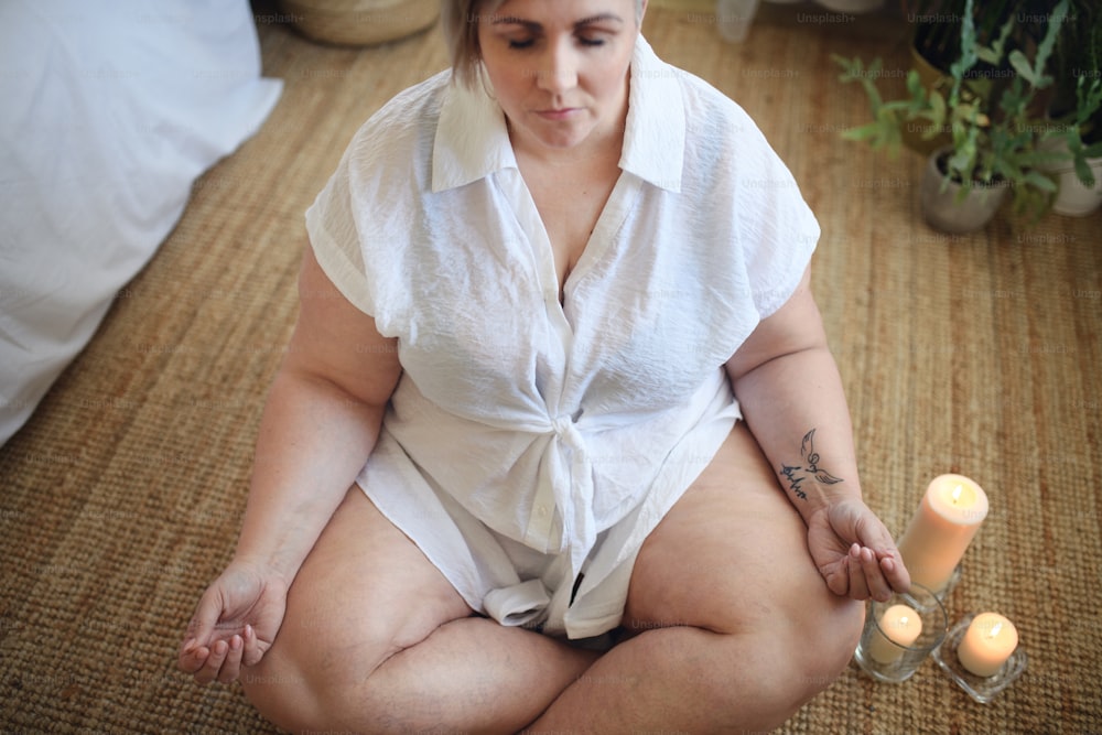 Un primo piano di una donna in sovrappeso che medita a casa.
