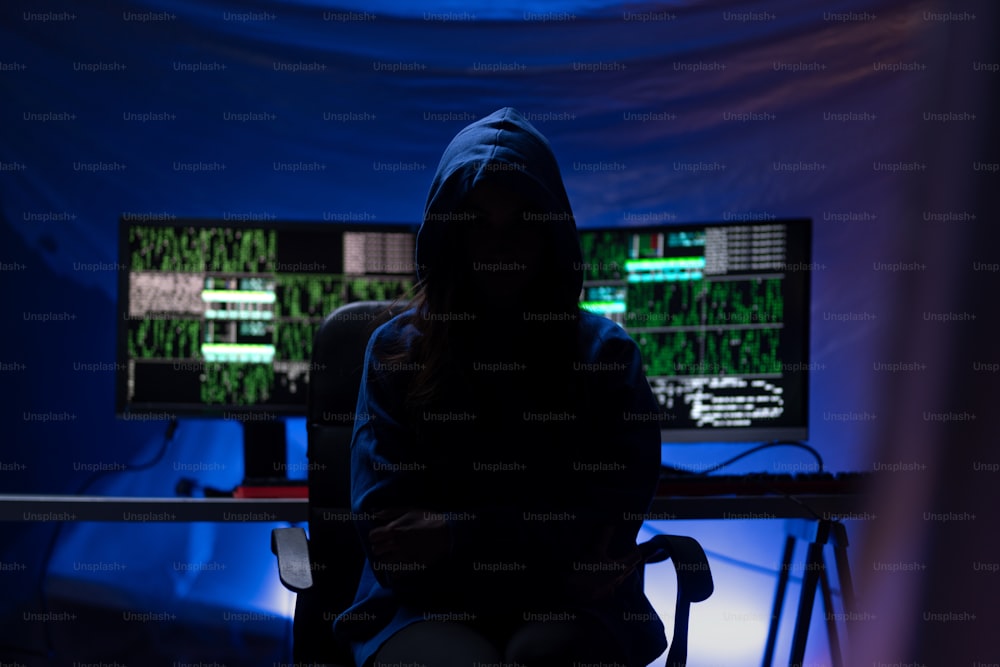 밤에 어두운 방에서 컴퓨터로 두건을 쓴 익명의 해커, 사이버 전쟁 개념.