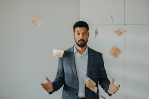A serious young businessman man standing in officethrowing money away, inflation concept.