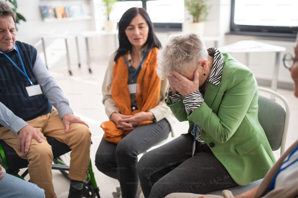 Um grupo de pessoas idosas sentadas em círculo durante a sessão de terapia, consolando a mulher deprimida.