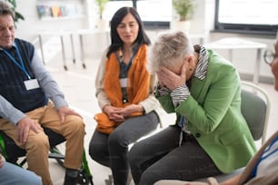 Un grupo de personas mayores sentadas en círculo durante la sesión de terapia, consolando a una mujer deprimida.