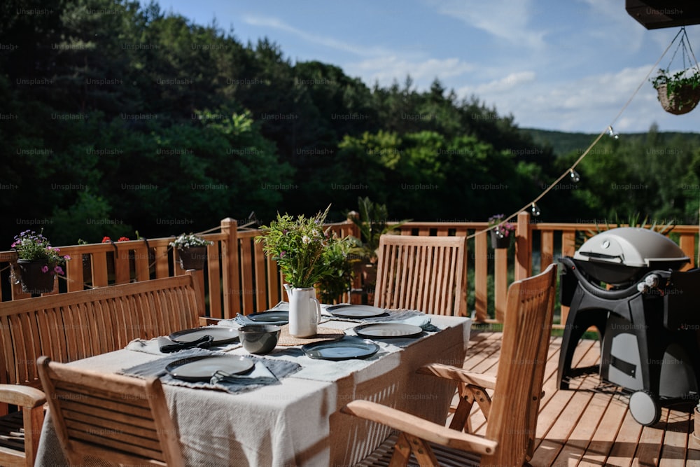 Un tavolo da pranzo con sedie in legno apparecchiato per la cena sulla terrazza con griglia in estate, festa in giardino. concetto.