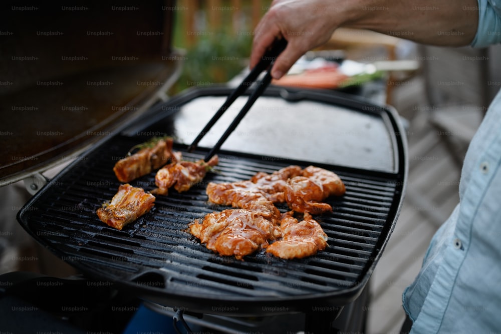 Un homme méconnaissable grillant de la viande, des côtes et des ailes, sur le gril pendant la garden-party d’été en famille, gros plan