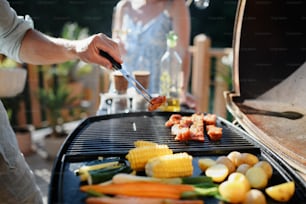 Un hombre irreconocible asando costillas y verduras a la parrilla durante una fiesta familiar de verano en el jardín