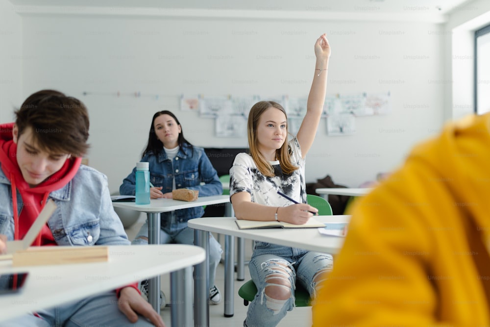 High school students paying attention in class, sitting in their desks and raising hands.