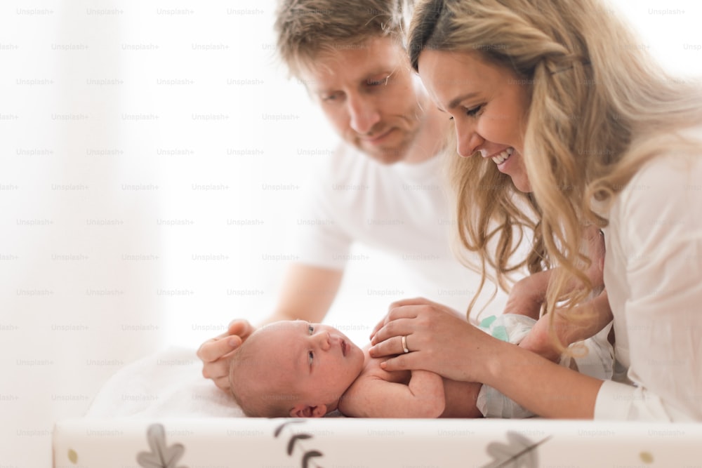 Happy parents bonding with their newborn son who is lying on a changing mat at home.