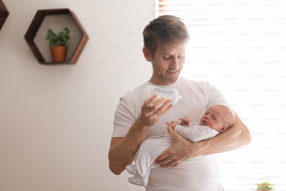 Un padre sosteniendo y alimentando a su hijo recién nacido con biberón en casa.